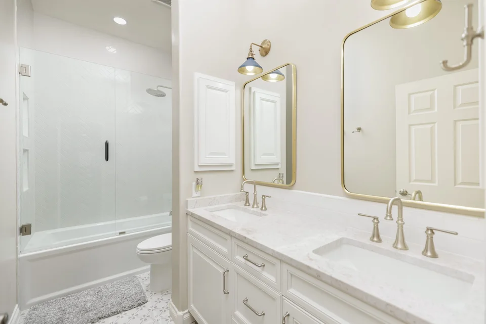 White double vanity with brass mirrors and a glass-enclosed tub