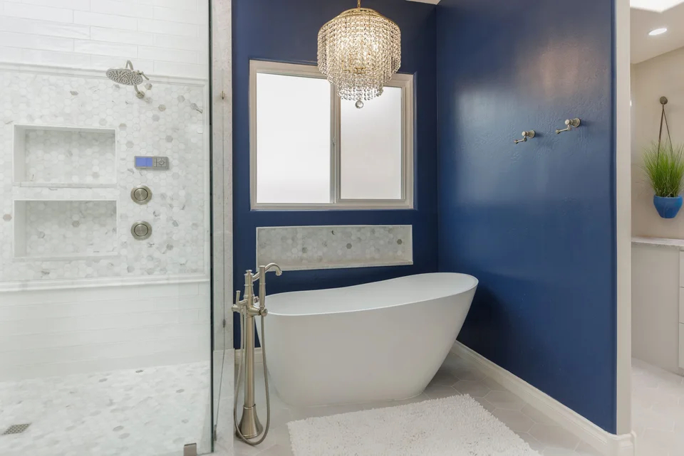 Freestanding white bathtub against navy walls beside a glass shower
