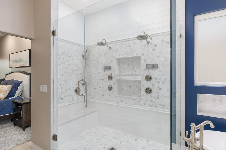 Glass-enclosed shower with pale tile and recessed niches