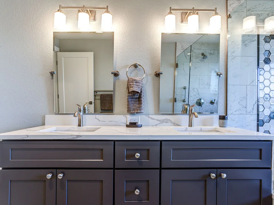 Dark double vanity with stone top and a glass shower in the mirror